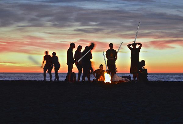 Festande människor med svärd grillar på en sandstrand